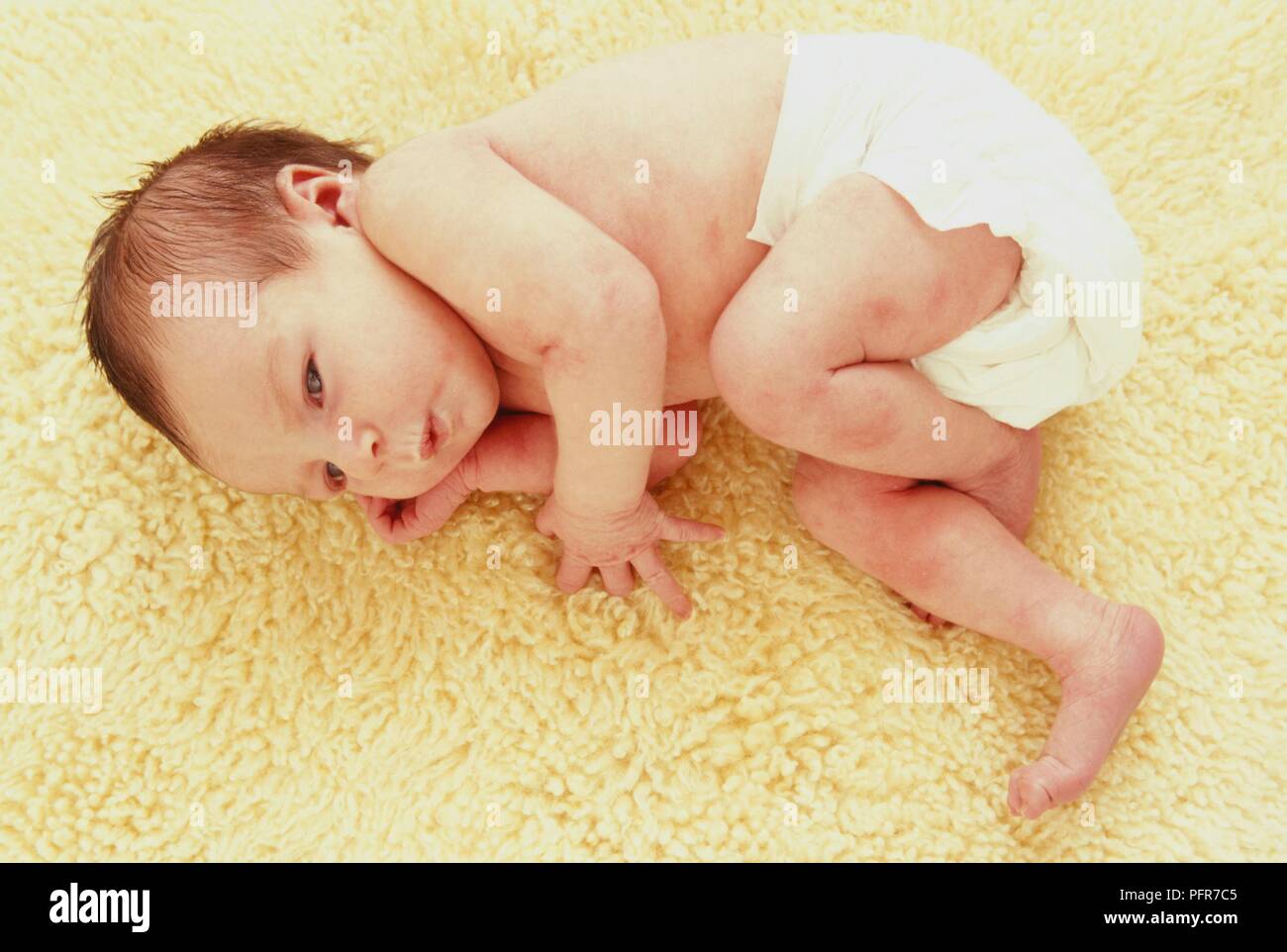 Neonato bambina indossa solo un pannolino giacente sul tappeto di pelle di pecora Foto Stock