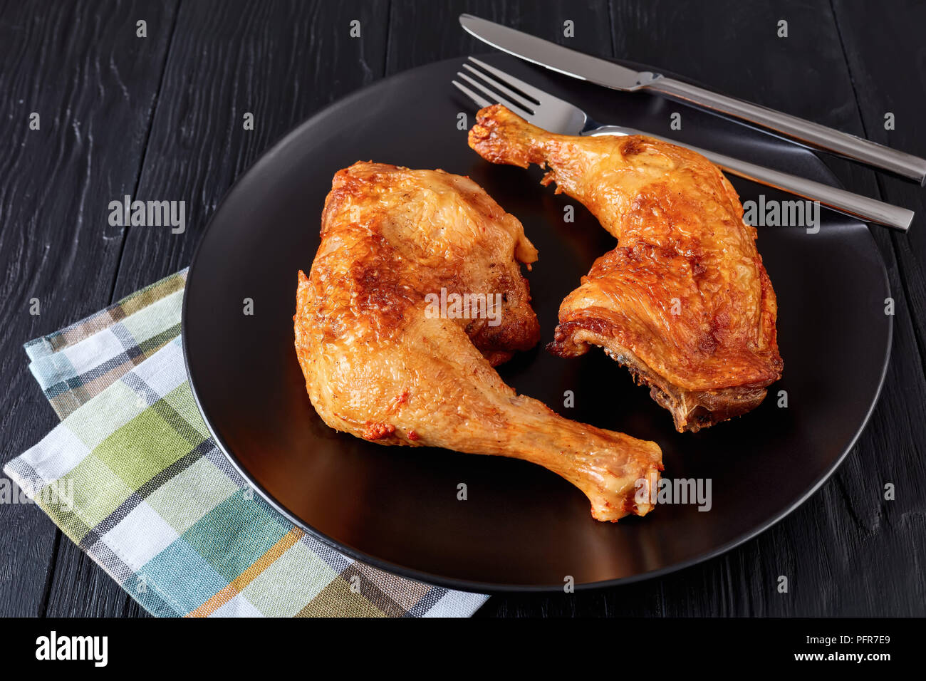 Close-up di pollo fritto gambe con golden pelle croccante servita su una piastra nera con coltello e forchetta su un tavolo di legno, orizzontale vista da sopra Foto Stock