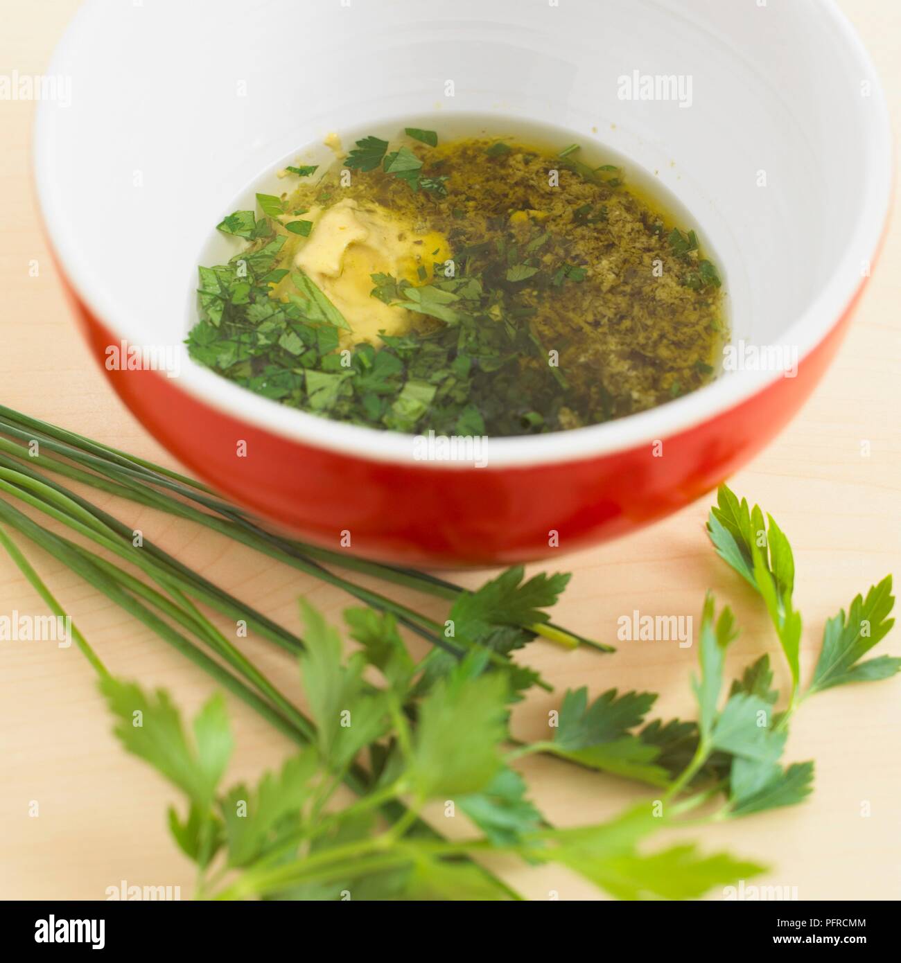 Ciotola di condimento per insalata contenente olio d'oliva, la mostarda, il pesto e il prezzemolo tritato, prezzemolo fresco accanto alla ciotola Foto Stock