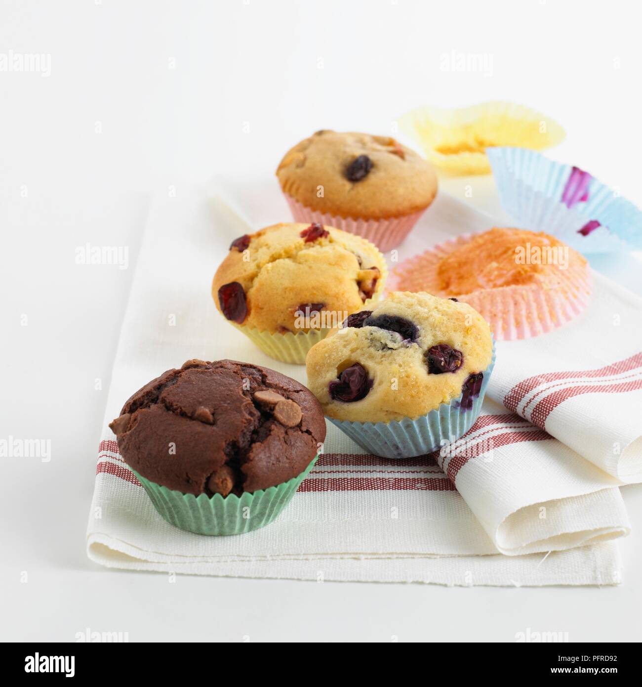 Una selezione di muffin su un canovaccio, compresi chocolate chip muffin, muffin ai mirtilli, cranberry muffin, raisin muffin, e casi di carta Foto Stock