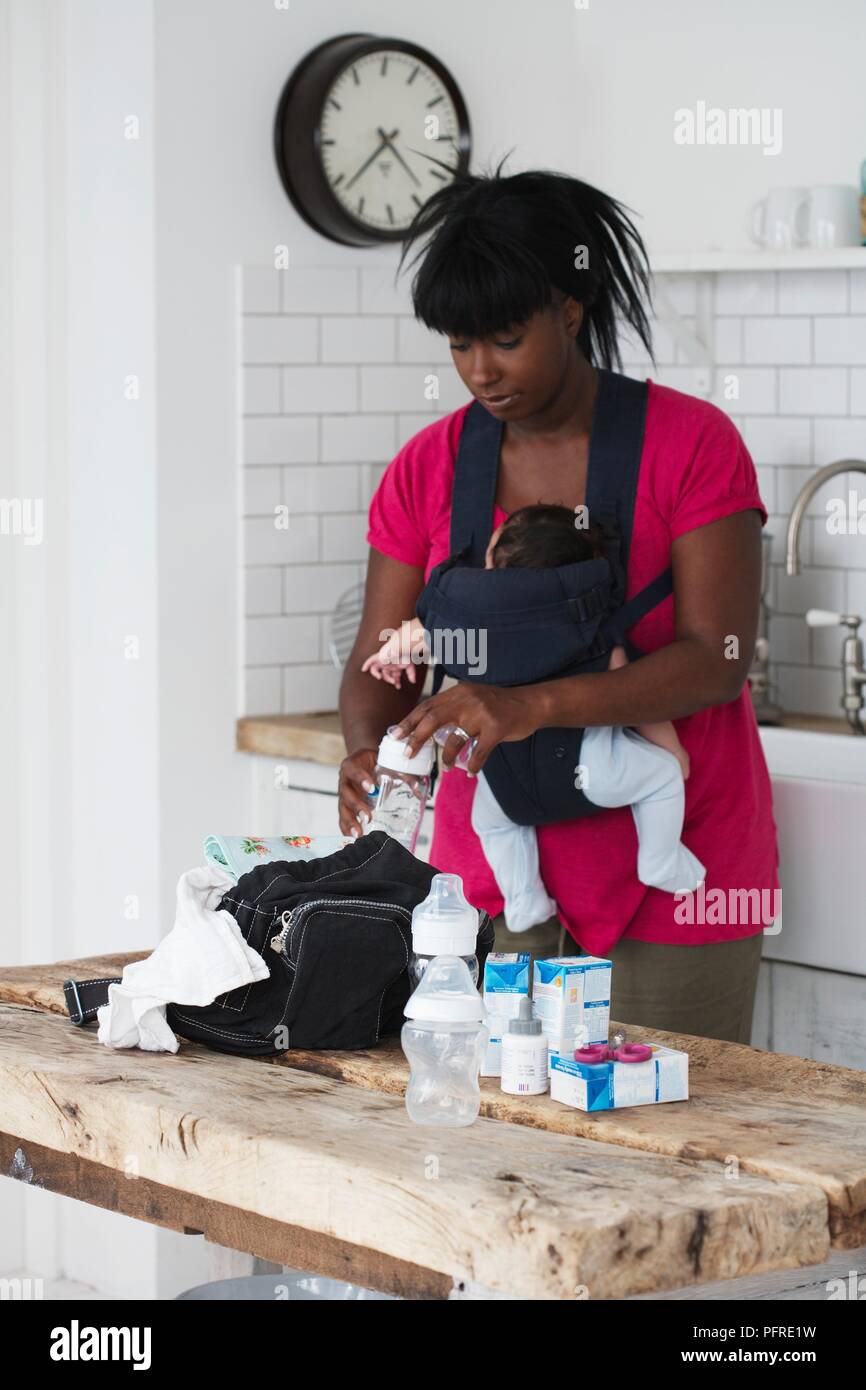 Donna imballaggio di un sacchetto in una cucina mentre si trasporta un bambino in un supporto anteriore Foto Stock