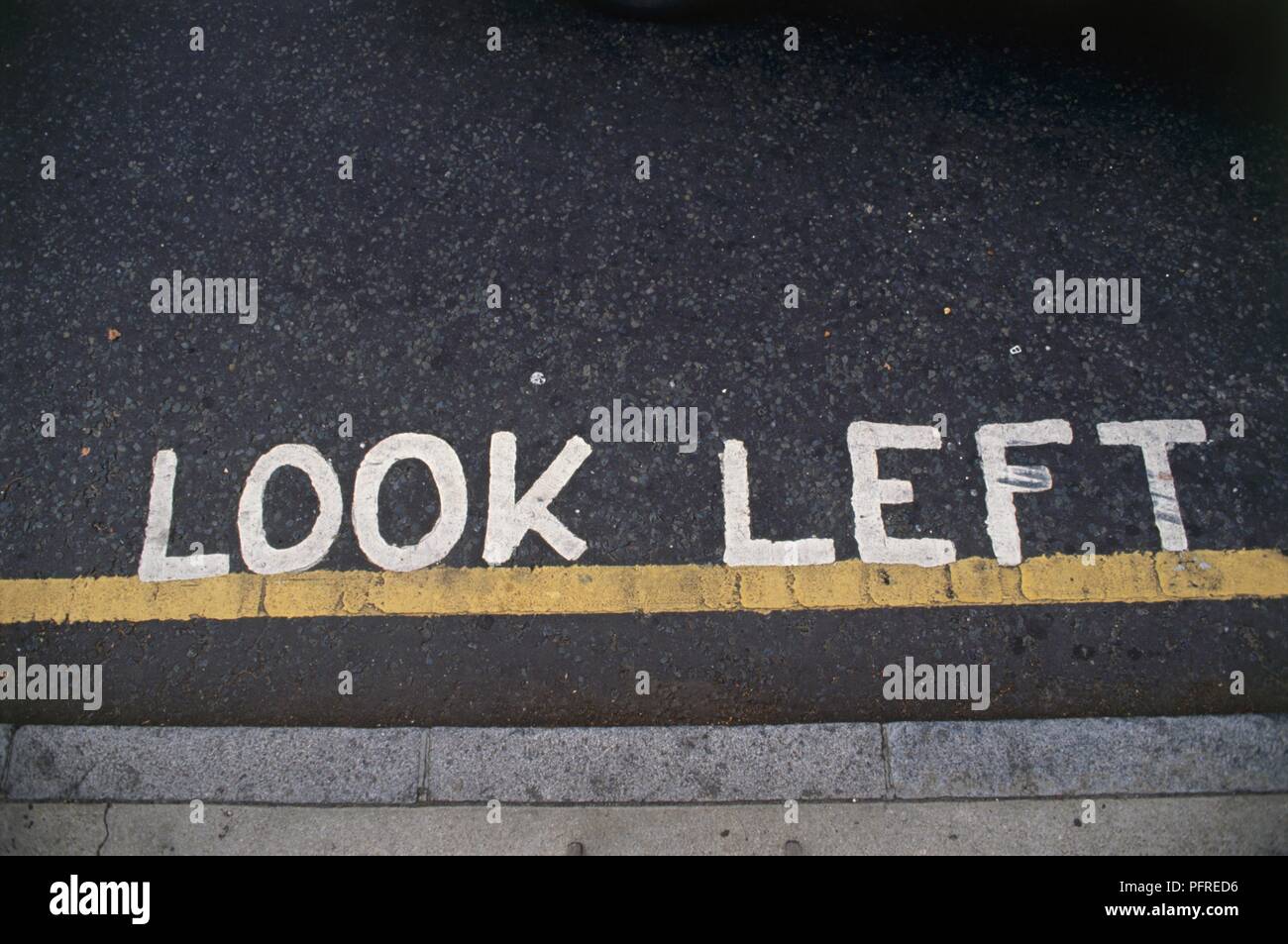 Gran Bretagna, Inghilterra, Londra, "Guardare a sinistra' scritta sulla strada, al di sopra della linea gialla, in prossimità del bordo del marciapiede Foto Stock