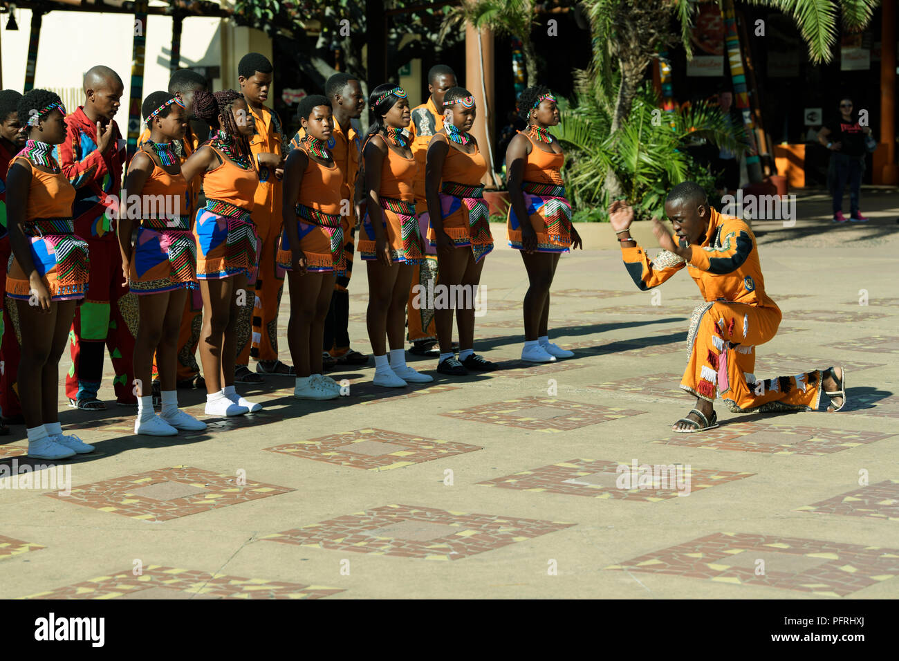 Giovane uomo Zulu in un colorato abito culturale di esibirsi di fronte a un gruppo di tradizionali degli artisti di strada a uShaka, Durban, Sud Africa Foto Stock