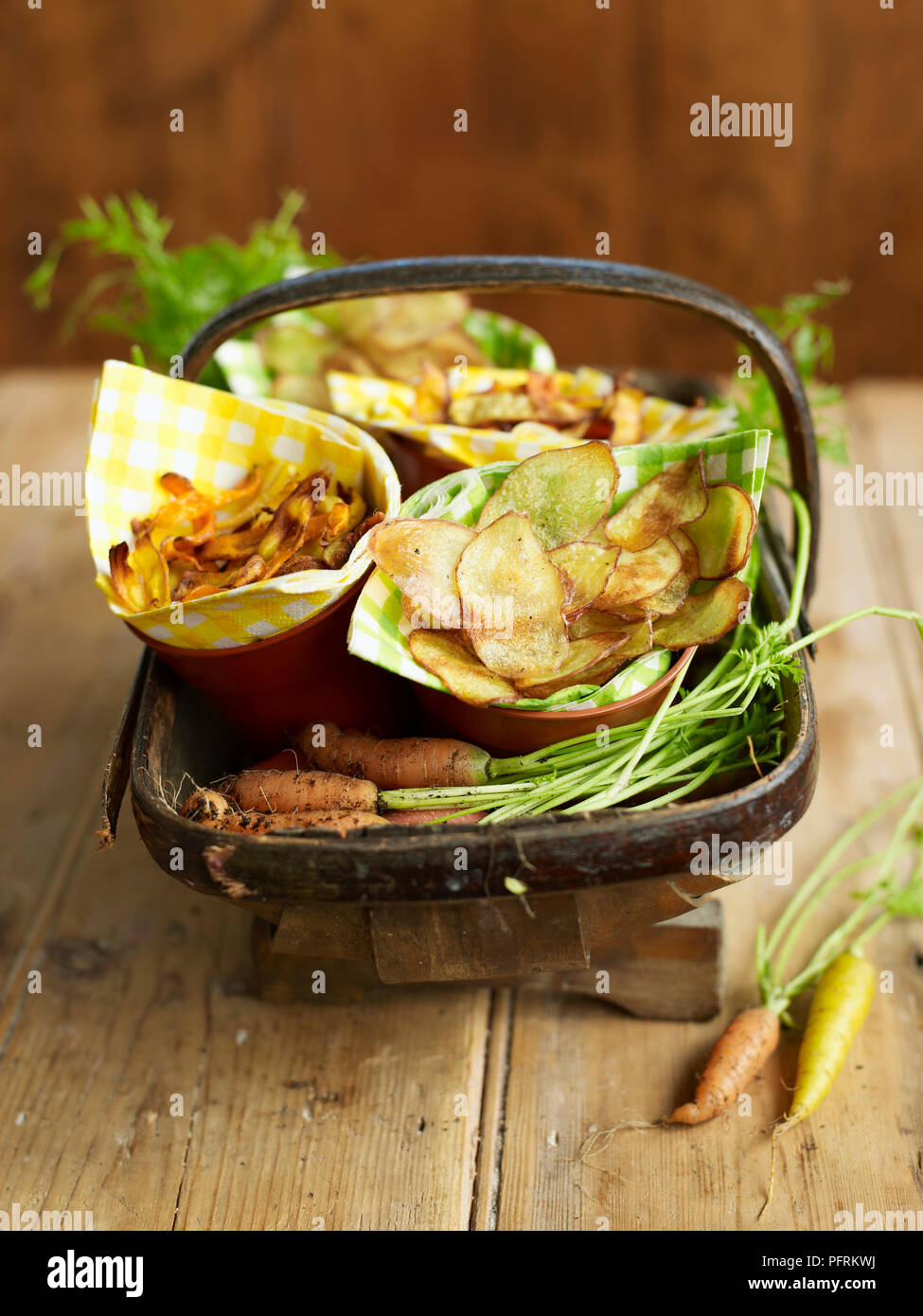Le carote e le patate e patatine vegetali avvolti in tovaglioli in vasi per piante in trug con materie prime carote sul tavolo di legno Foto Stock