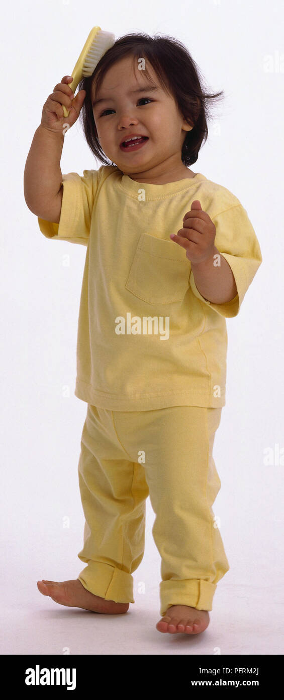 Bimbi a piedi nudi indossando la parte superiore gialla e pantaloni spazzolare i capelli con spazzola per capelli Foto Stock