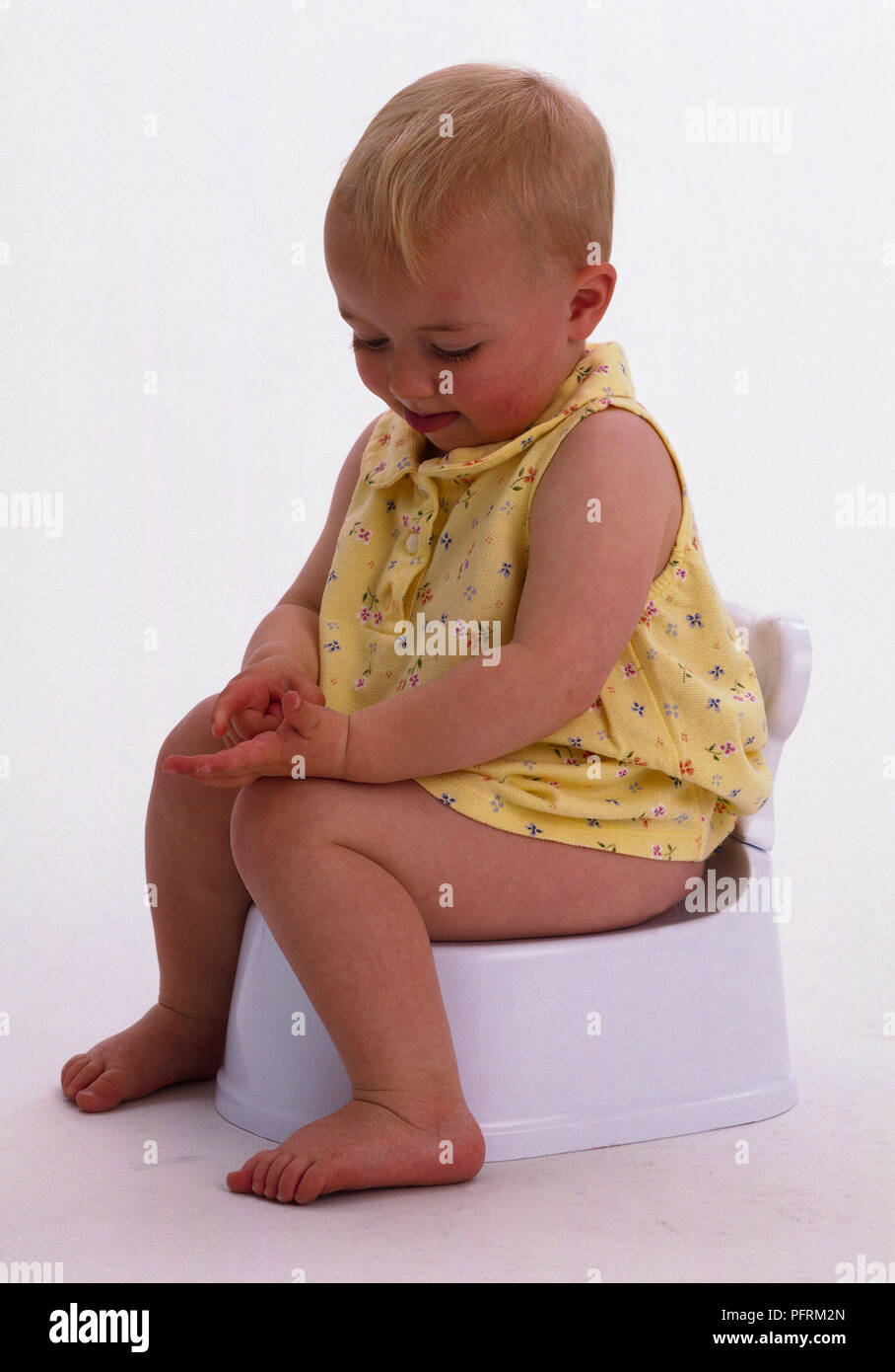Il Toddler indossando giallo abito floreale seduta sul vasino Foto Stock