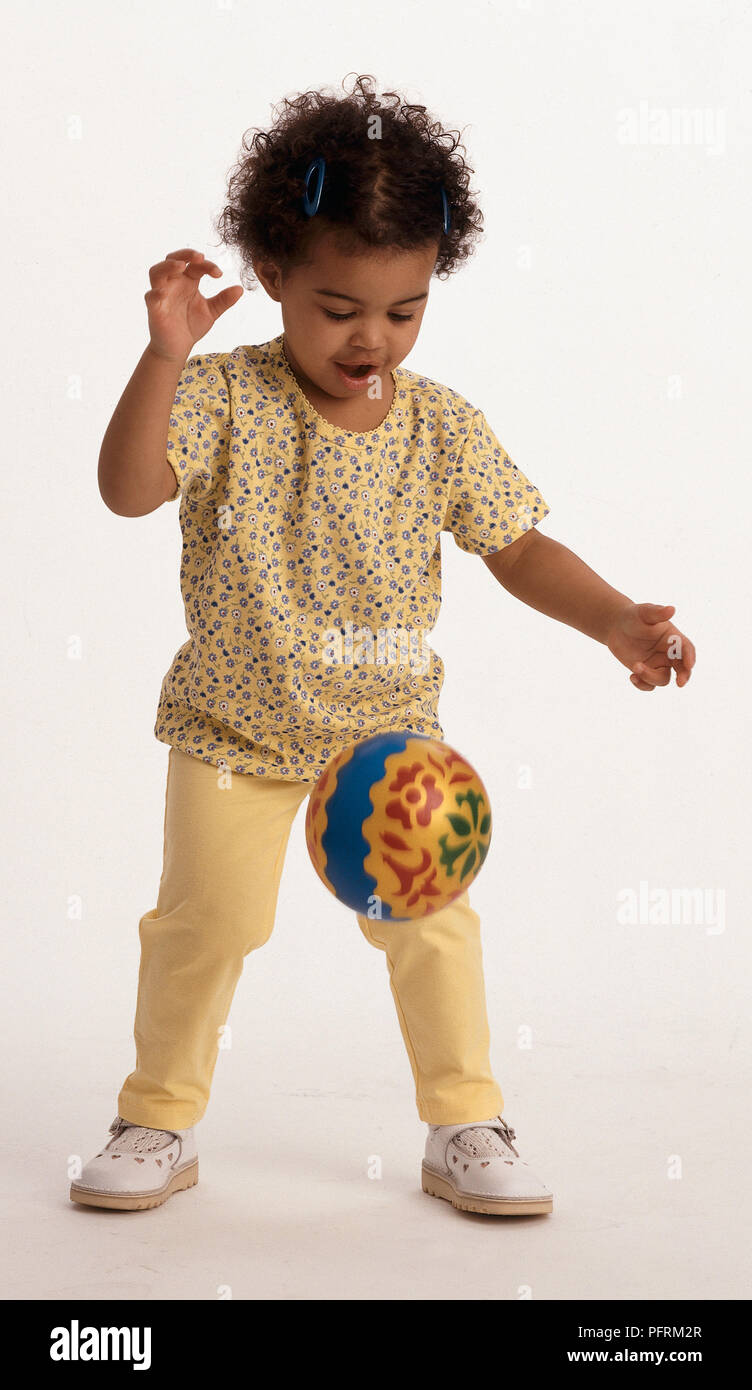 Il Toddler indossando giallo motivo floreale top e pantaloni gialli, guardando la pallina che rimbalza Foto Stock