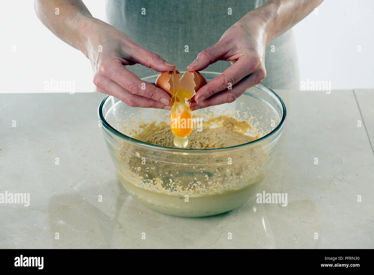 La rottura delle uova al di sopra della vaschetta di miscelazione contenente miscela per torte Foto Stock