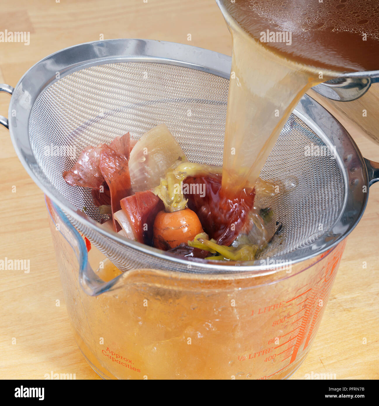 Versare il brodo di carne attraverso il setaccio in caraffa di vetro, la cattura di pezzi di cipolla, cime di carota e sedano, close-up Foto Stock