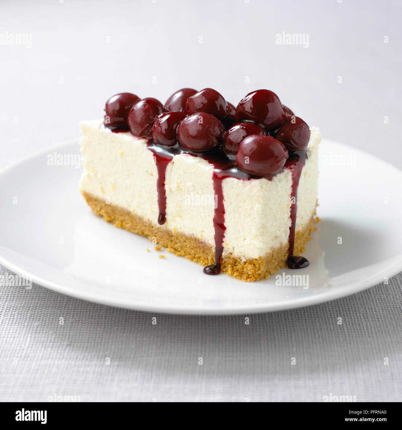 Fetta di amarena cheesecake con succo gocciolamento verso il basso i lati sulla piastra bianca Foto Stock