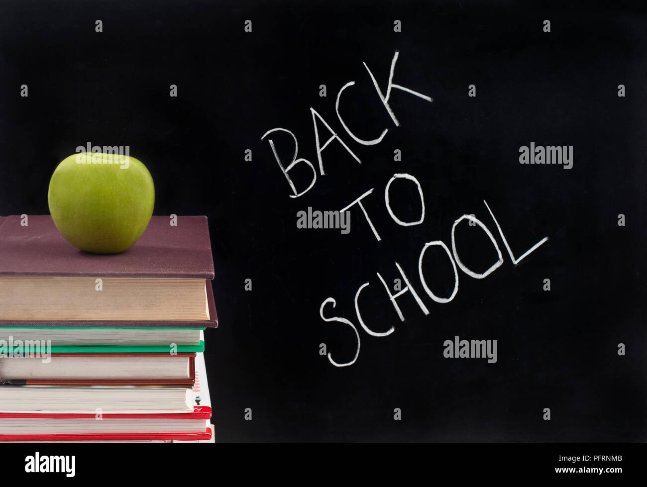 La frase "Si torna a scuola" scritto in gesso su una lavagna, accanto a una pila di libri con un Apple sulla parte superiore Foto Stock