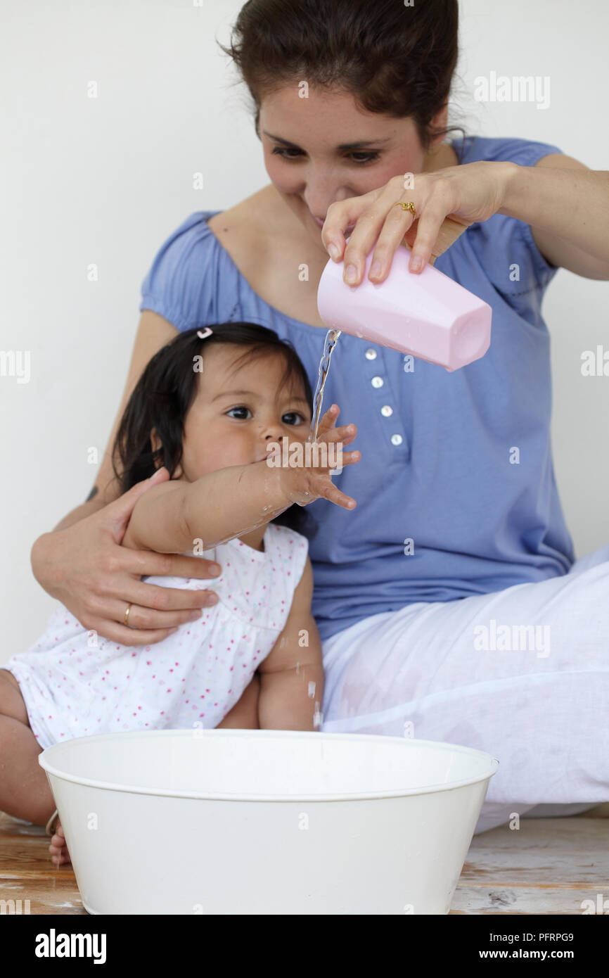 Donna versando acqua dalla coppa over mano della bambina (11 mesi) Foto Stock
