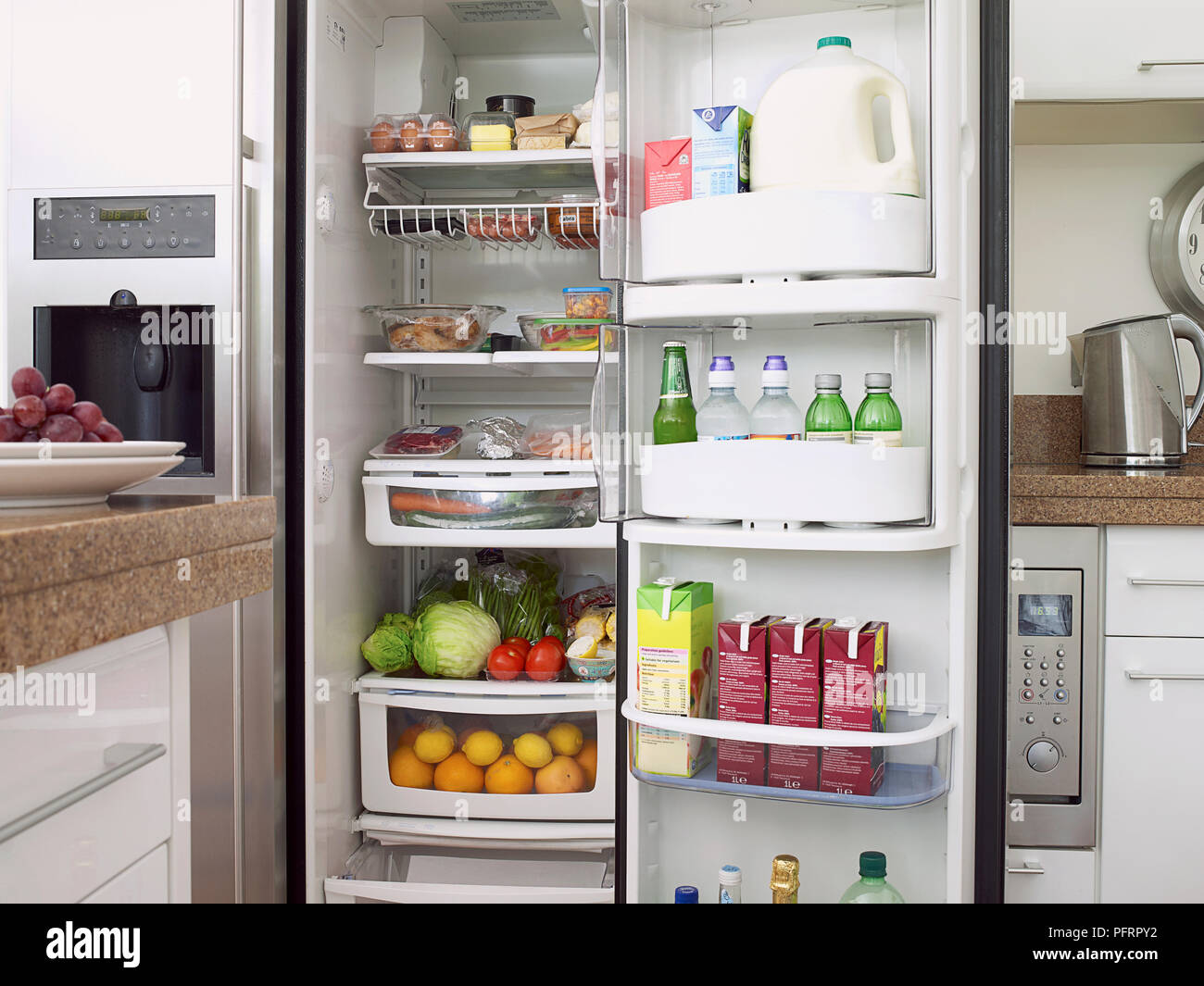 Mangiare e bere in pieno frigorifero domestico con lo sportello aperto Foto Stock
