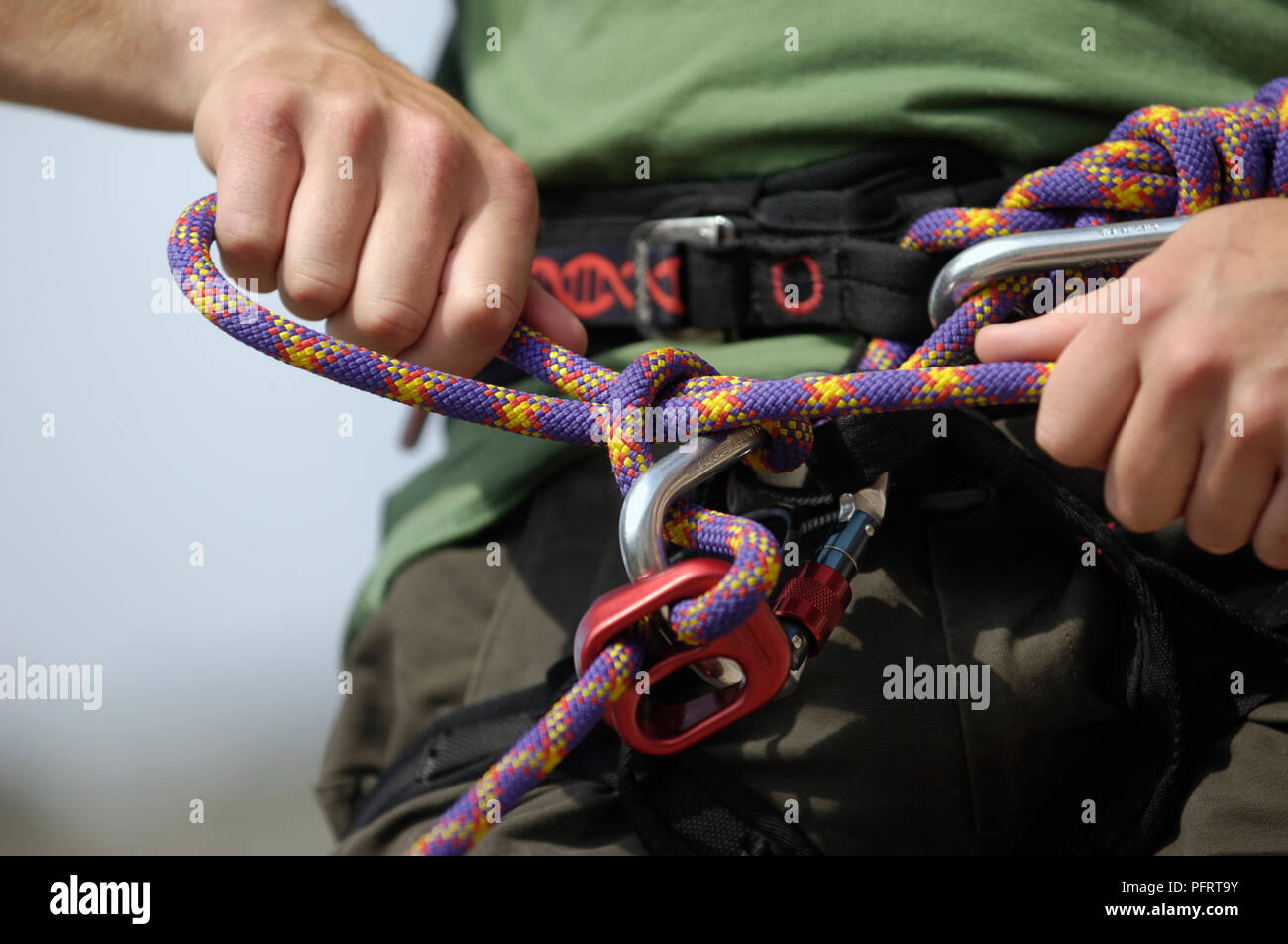 Maschio di scalatore insenatura di threading di arrampicata corda attraverso il primo anello e tirando stretta a formare il nodo del sollevatore, close-up Foto Stock