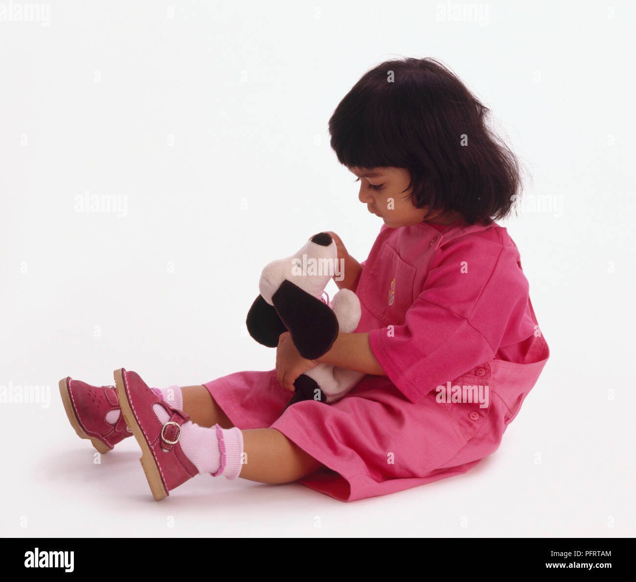 Il Toddler indossare top rosa, salopette da sandali e seduto sul pavimento tenendo in bianco e nero cane Foto Stock