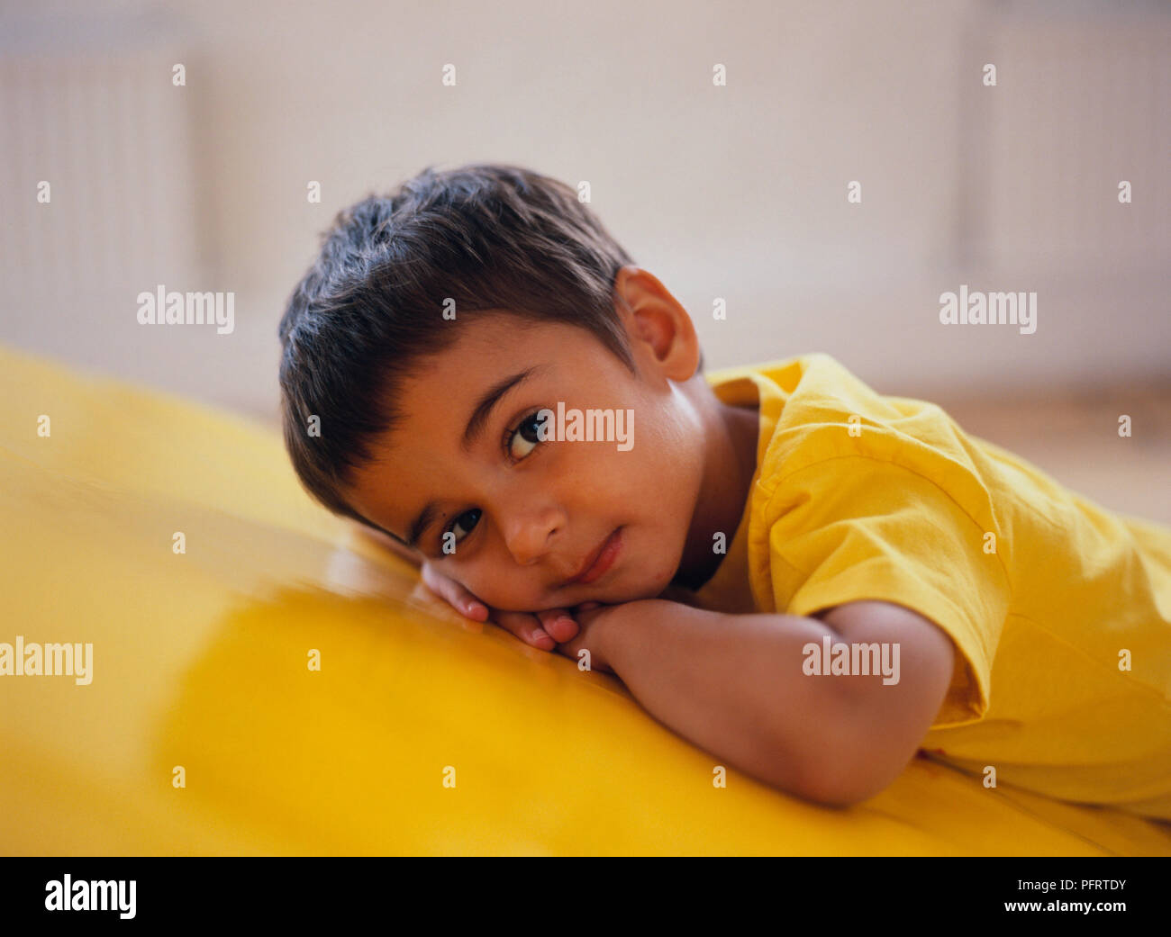Stanco toddler giallo che indossa la t-shirt in appoggio sul giallo cuscino in plastica Foto Stock