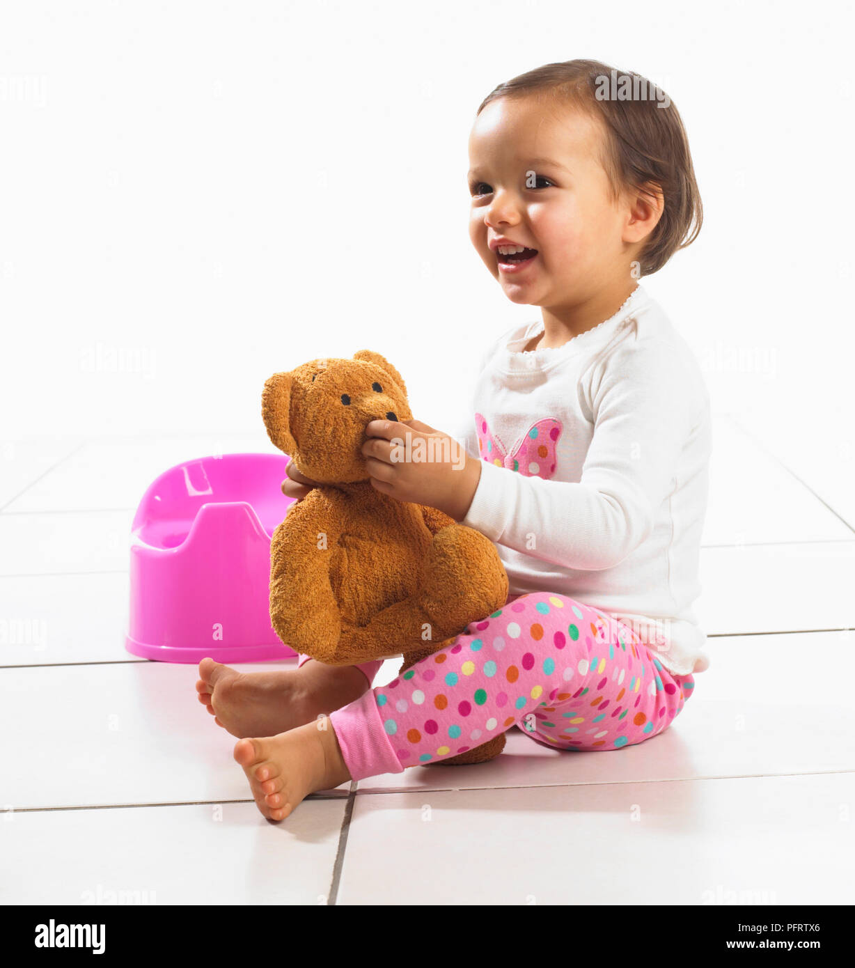 Il Toddler girl holding giocattolo morbido, vasino in background, 1,5 anni Foto Stock