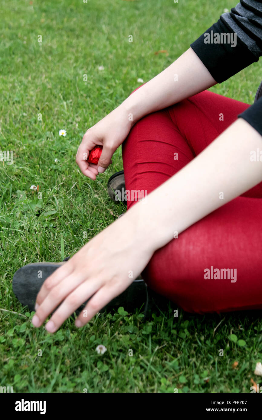 Giovane donna indossa gambali rosso sat sull'erba Foto Stock