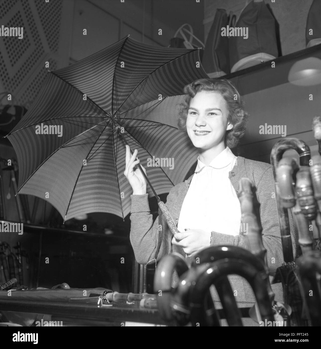 Ombrelloni negli anni cinquanta. Una giovane donna è lavorare in un negozio come un salesclerk. Ella dimostra uno degli ombrelloni per un cliente. S. Steéns Speceri & Diversehandel Svezia 1952 ref 2252 Foto Stock
