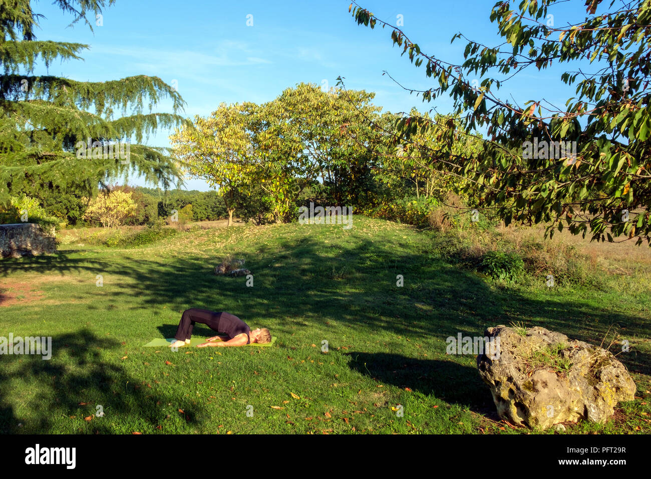 Circondato dalla campagna idilliaca campagna francese una donna matura la sua prassi posizioni di yoga in autunno bello e mite sole. La posa del ponte. Foto Stock