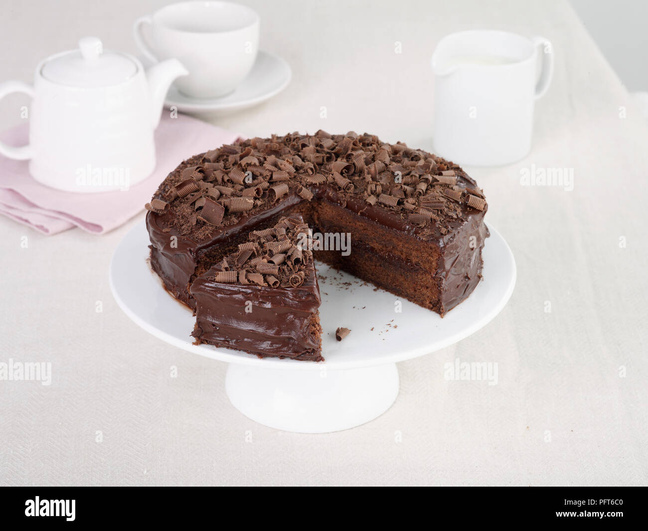 Devil's torta servito sulla torta stand con brocca di crema, teiera e tazza dietro Foto Stock