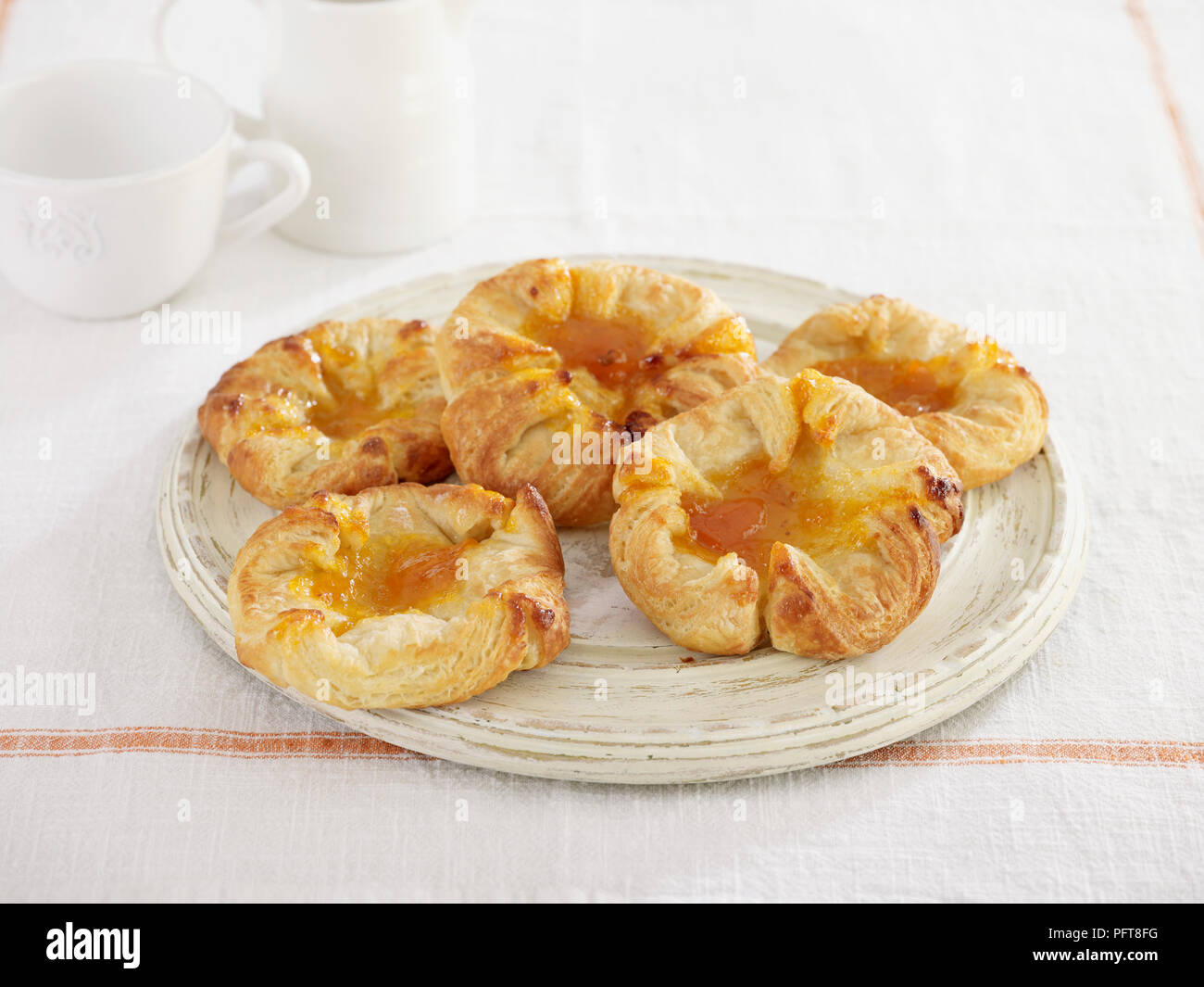 Albicocca pasticceria danese servita su piastra, brocca e tazza dietro Foto Stock