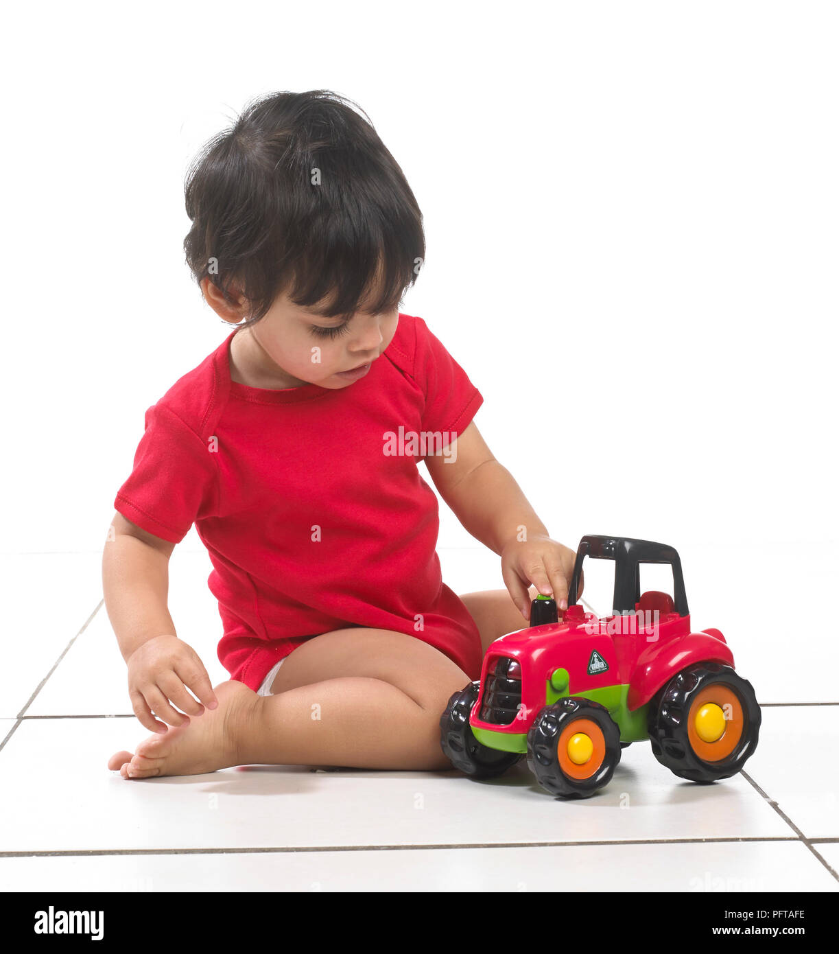 Baby boy (16 mesi) seduta con trattore giocattolo Foto Stock