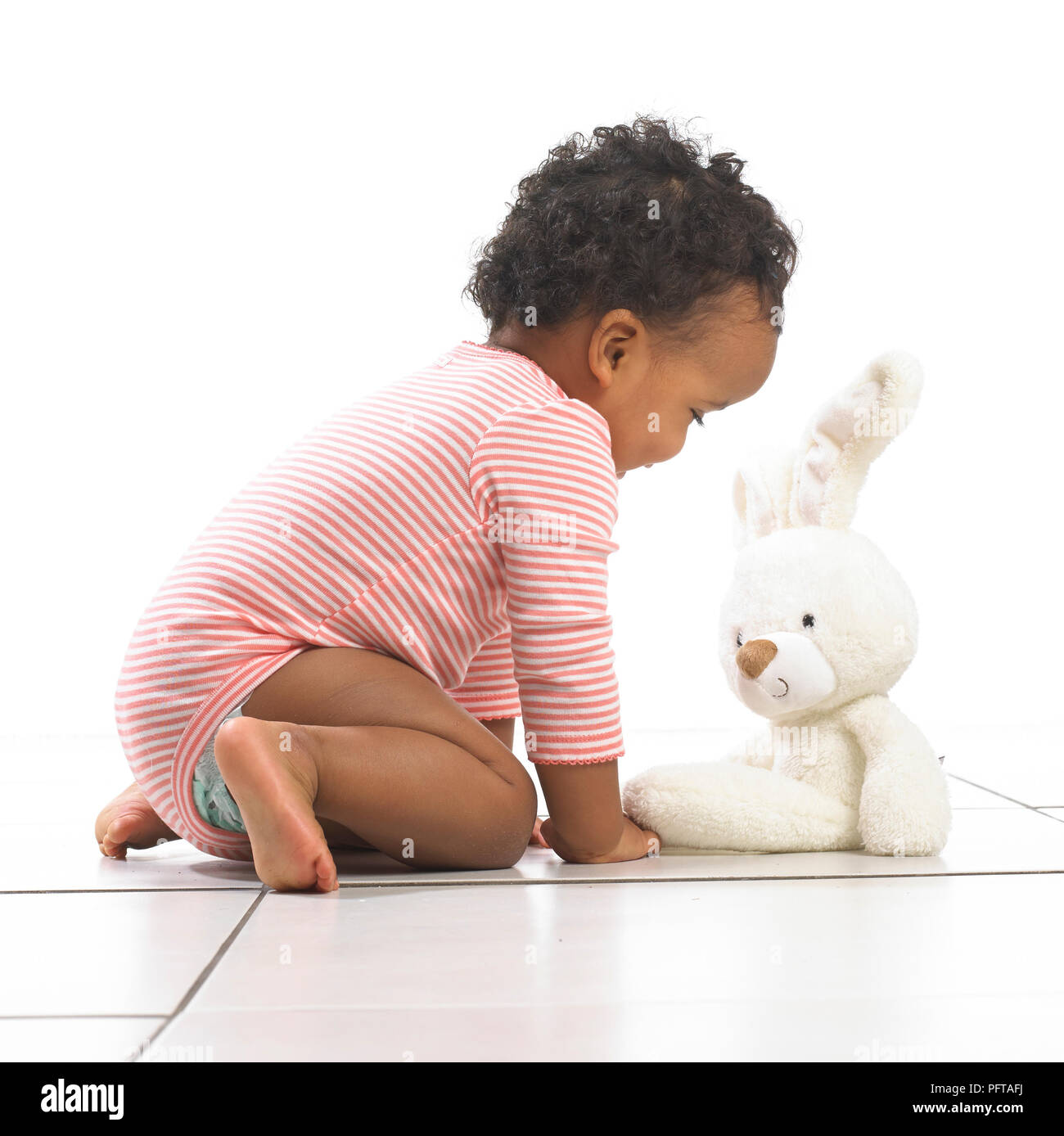 Ragazza inginocchiata verso un giocattolo di coniglio, 18 mesi Foto Stock