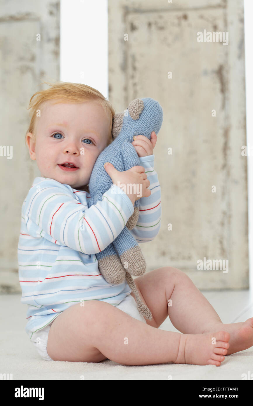 Baby boy cuddling morbida maglia monkey toy, dodici mesi Foto Stock