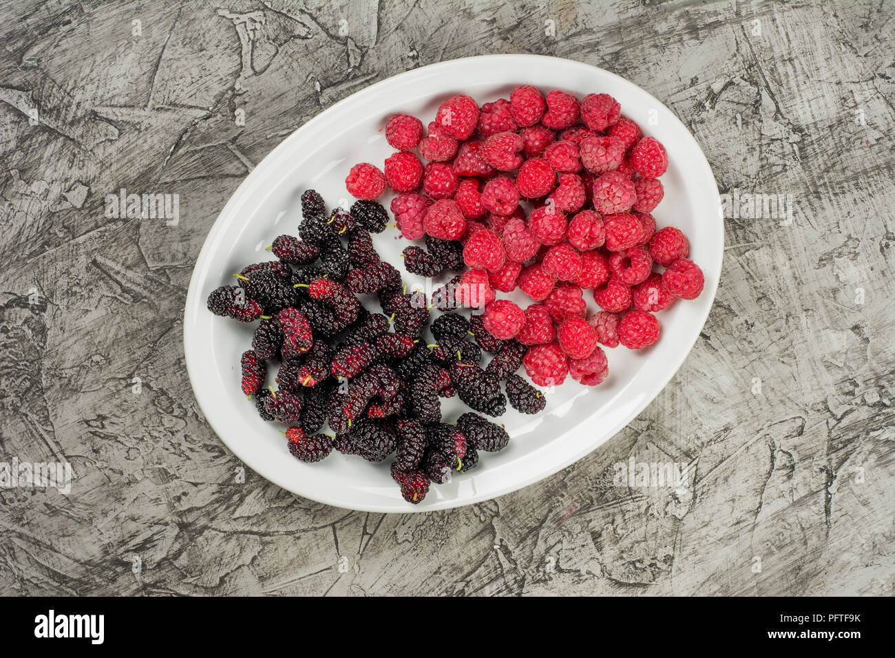 Piastra con lamponi e Mulberry. Frutti di bosco freschi su calcestruzzo sfondo vista superiore Foto Stock