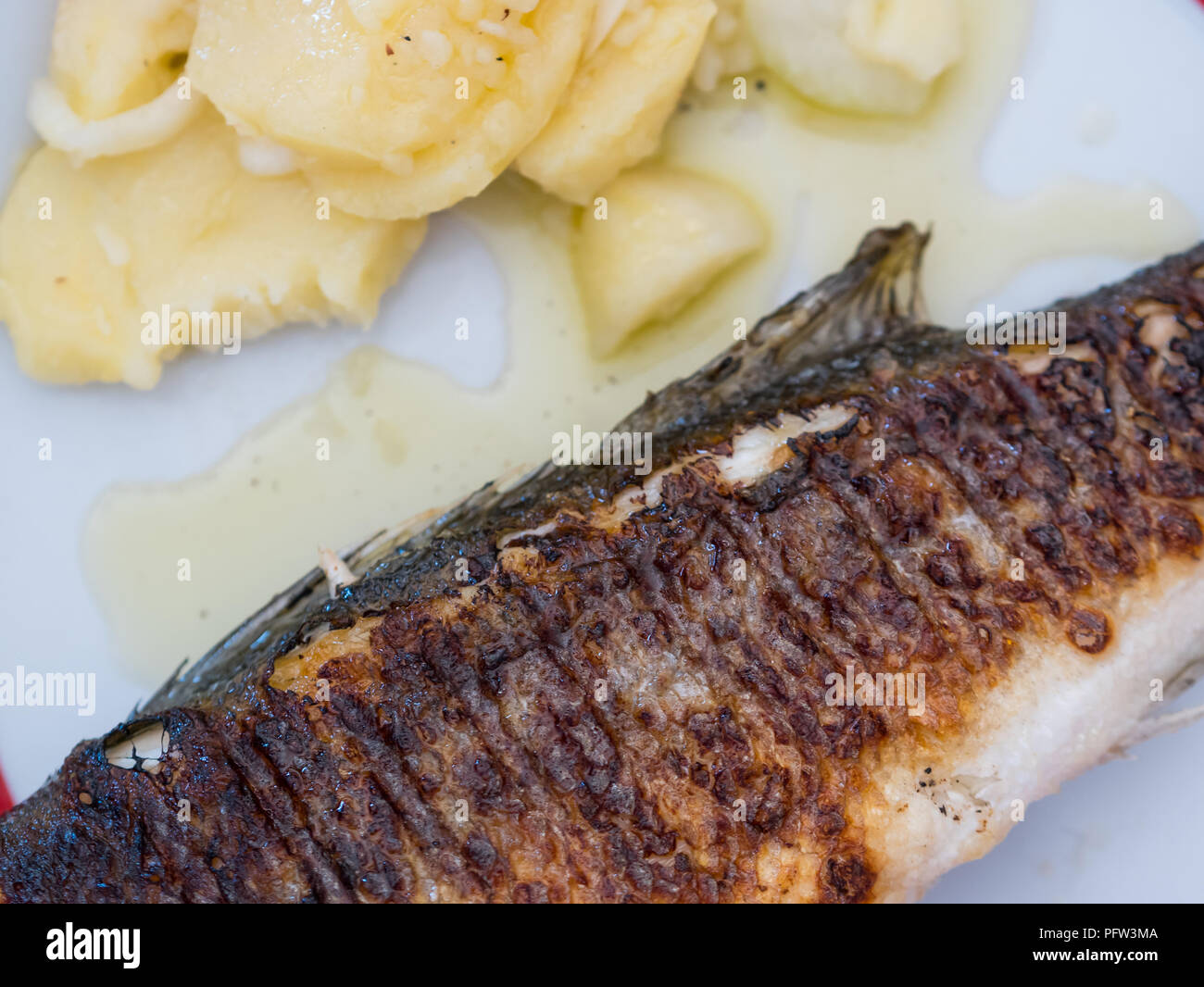 Tutta la spigola pesce e insalata di patate sulla piastra per pranzo vista superiore Foto Stock