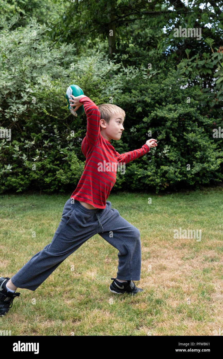 10 anno vecchio ragazzo gettare un calcio sul suo prato Foto Stock