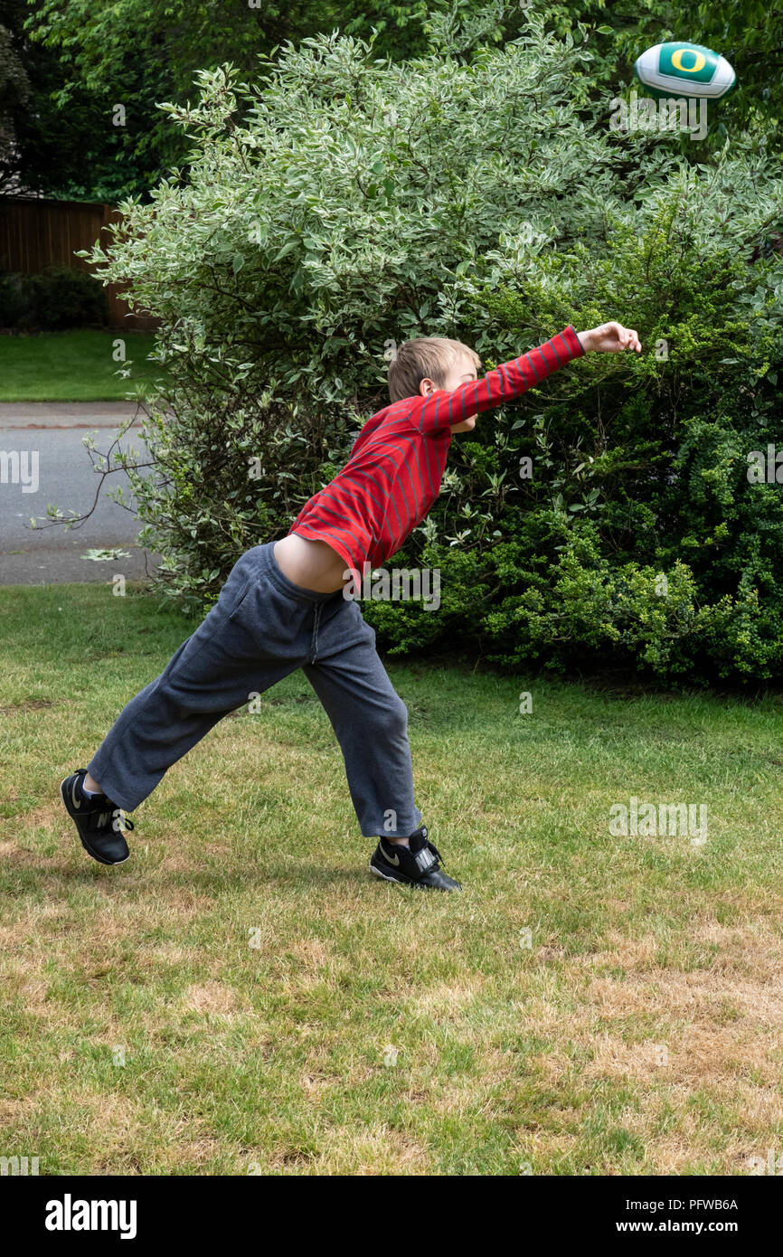 10 anno vecchio ragazzo gettare un calcio sul suo prato Foto Stock