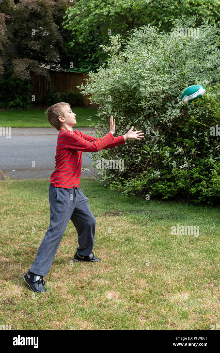 10 anno vecchio ragazzo cerca di catturare un pallone da calcio Foto Stock