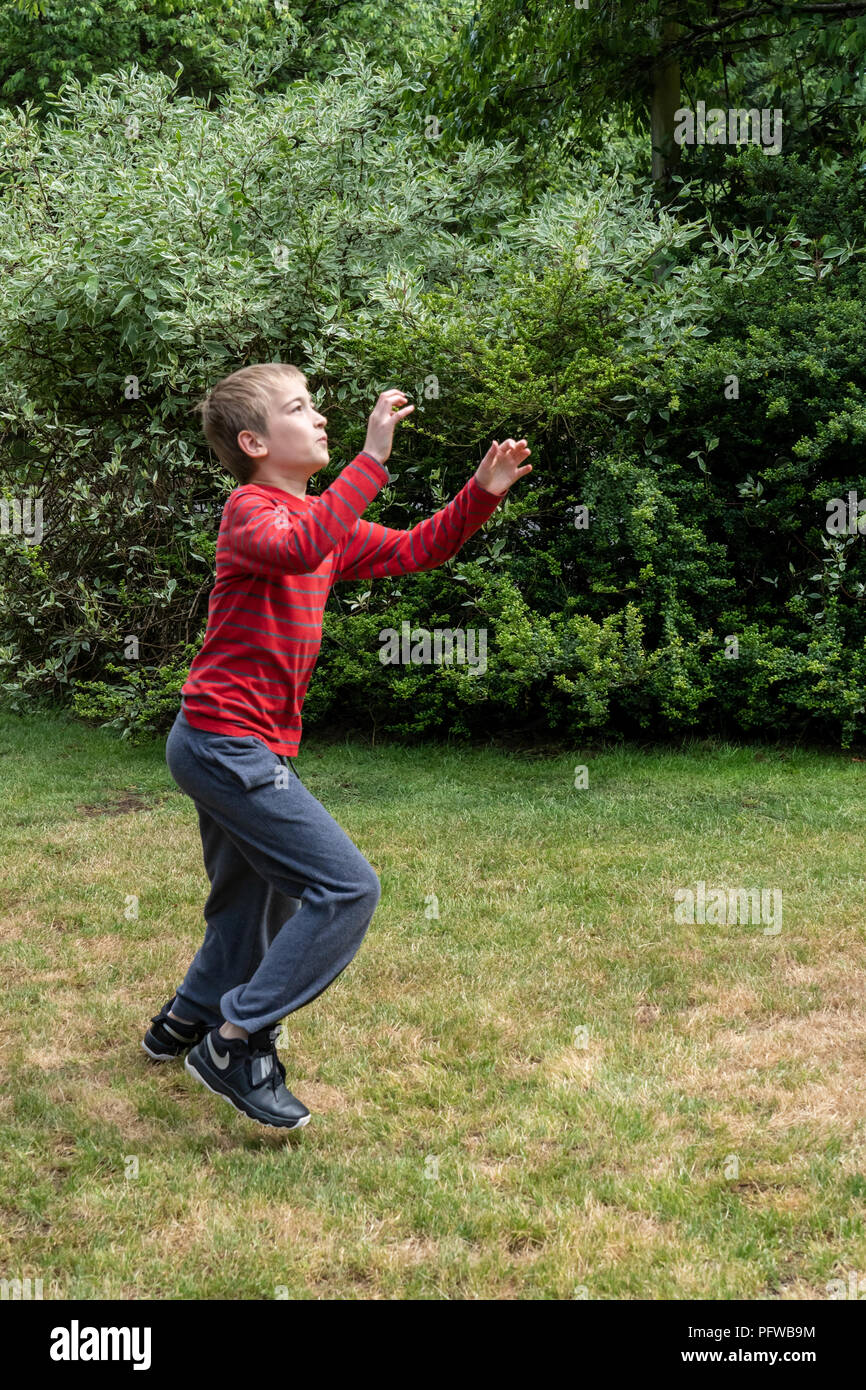 10 anno vecchio ragazzo lo spostamento in posizione per la cattura di un pallone da calcio che è stato gettato sul suo prato Foto Stock