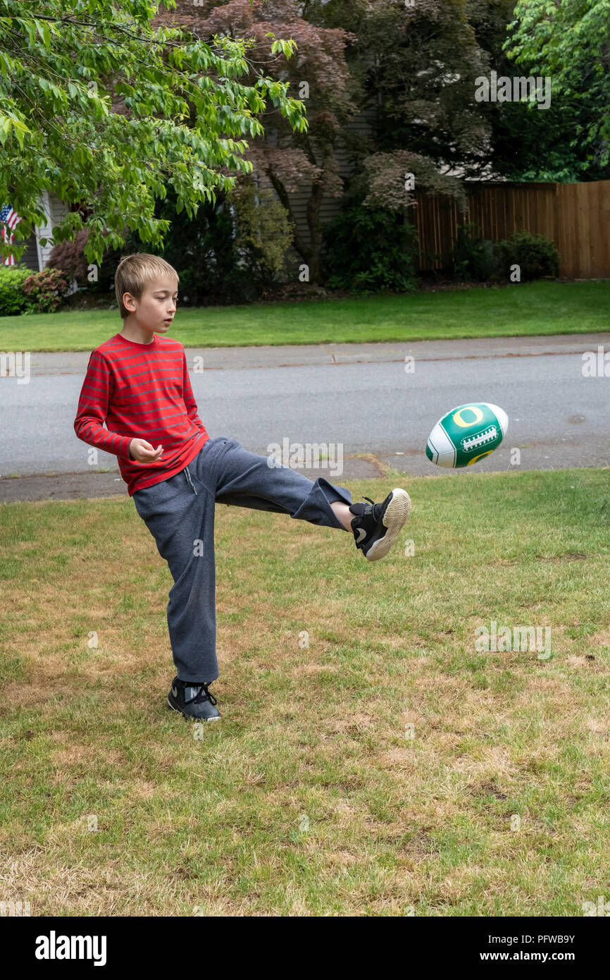 10 anno vecchio ragazzo calci un calcio sul suo prato Foto Stock