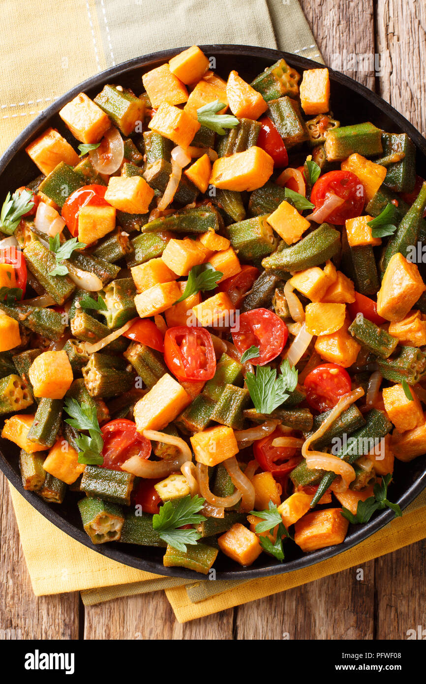 Stufato di vegetali okra, patate dolci, pomodori, cipolle ed erbe closeup su una piastra sul tavolo. Verticale in alto vista da sopra Foto Stock