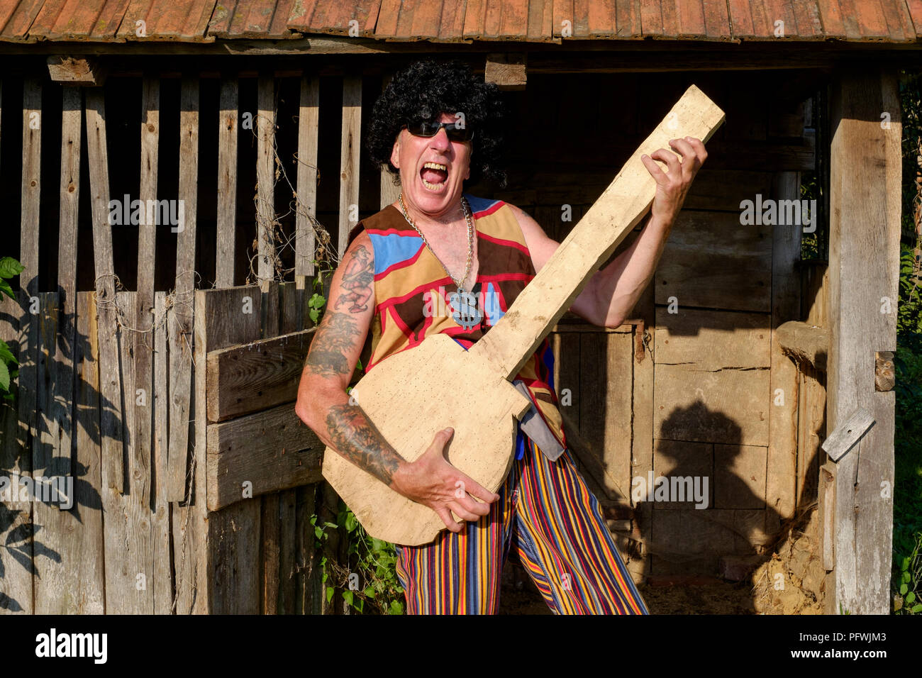 Effettuare lo spoofing ritratto di maschi più anziani parrucca da indossare occhiali da sole luminoso e abbigliamento medaglione durante la riproduzione di un fake guitar metà di vita il concetto di crisi Ungheria Foto Stock