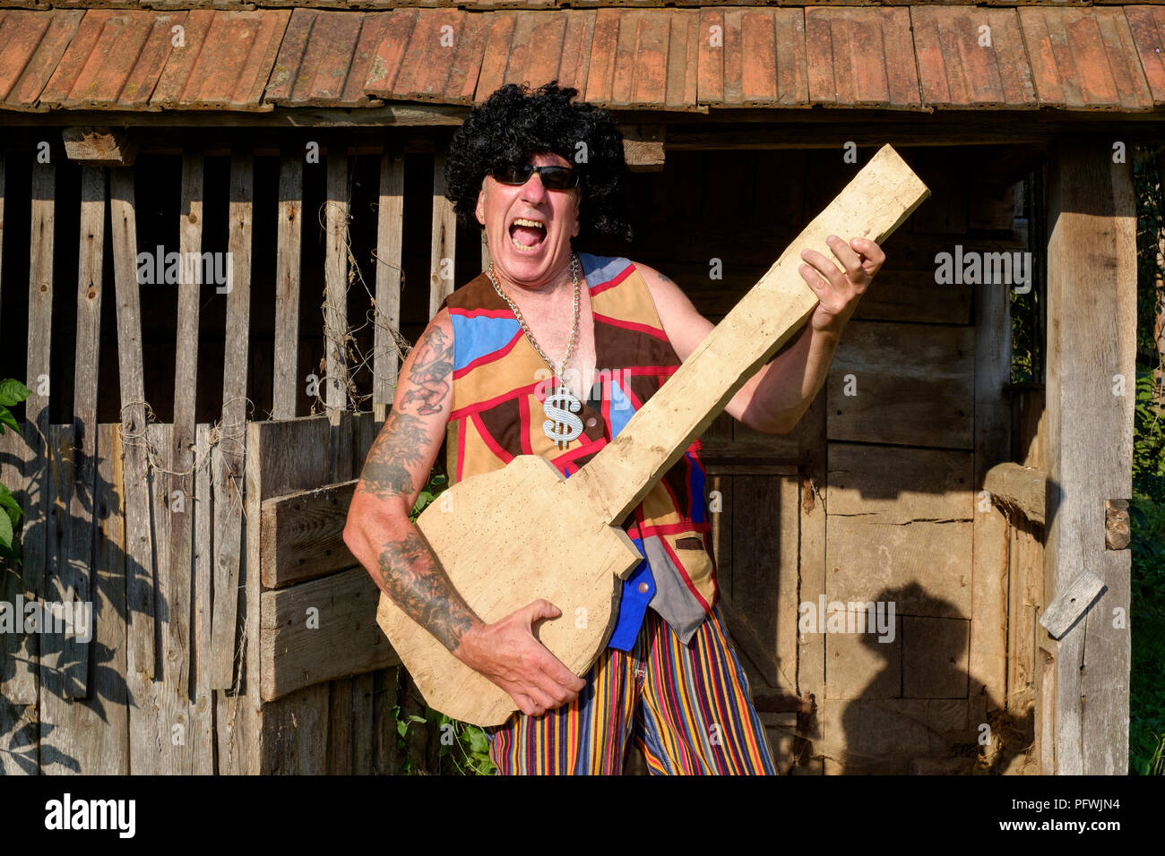 Effettuare lo spoofing ritratto di maschi più anziani parrucca da indossare occhiali da sole luminoso e abbigliamento medaglione durante la riproduzione di un fake guitar metà di vita il concetto di crisi Ungheria Foto Stock