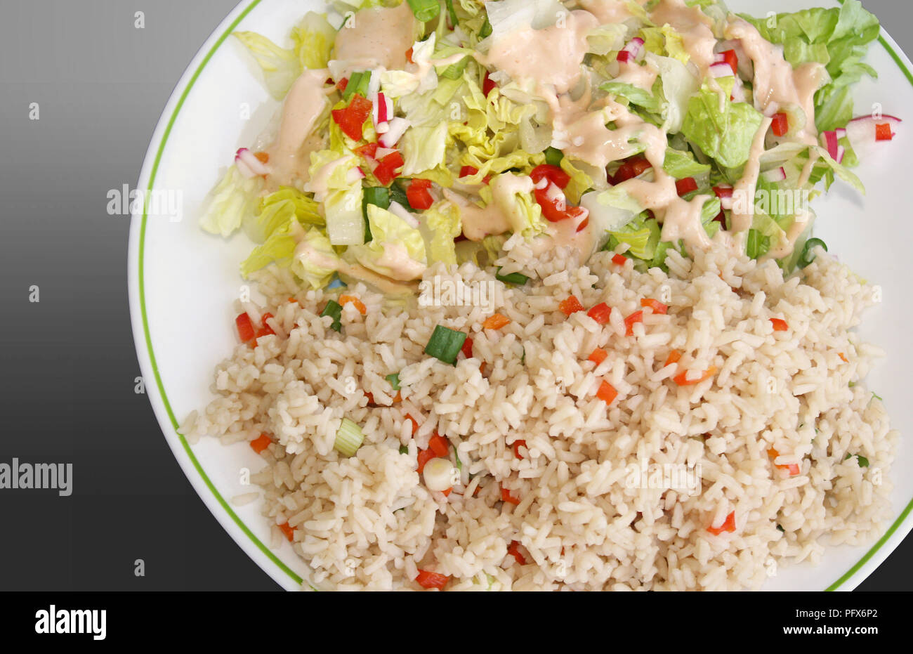 Pasto sano dei cereali integrali riso marrone con verdure e un fresco giardino insalata condito con un condimento di consistenza cremosa Foto Stock