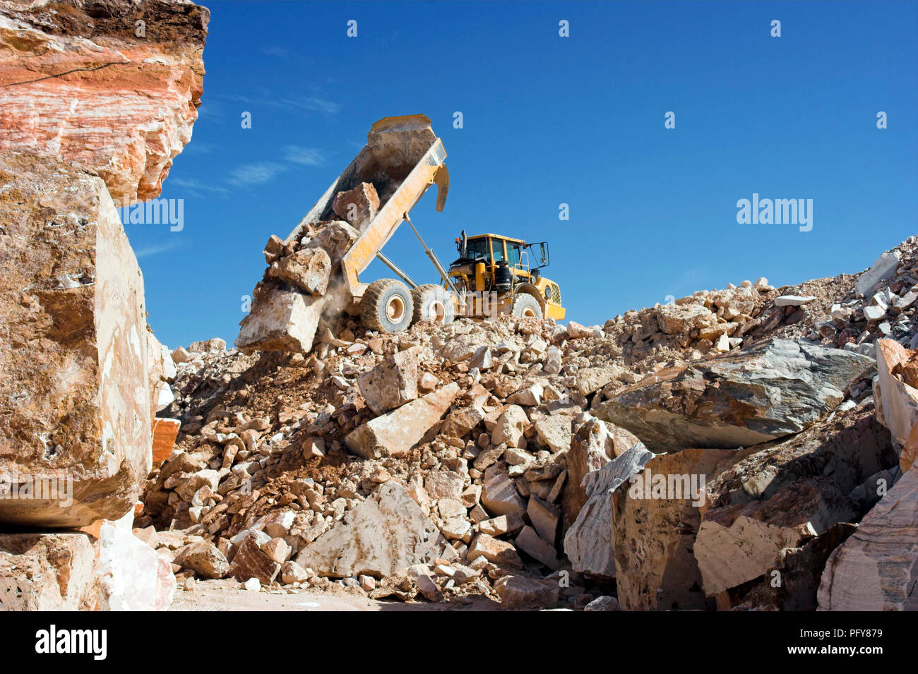 Heavy camion contro il cielo blu che operano in una cava di marmo Foto Stock