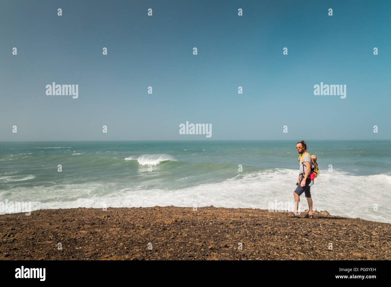 Uomo che cammina con il bambino sulla schiena in tutta la spiaggia a Fuerteventura, Isole Canarie, Spagna. Foto Stock