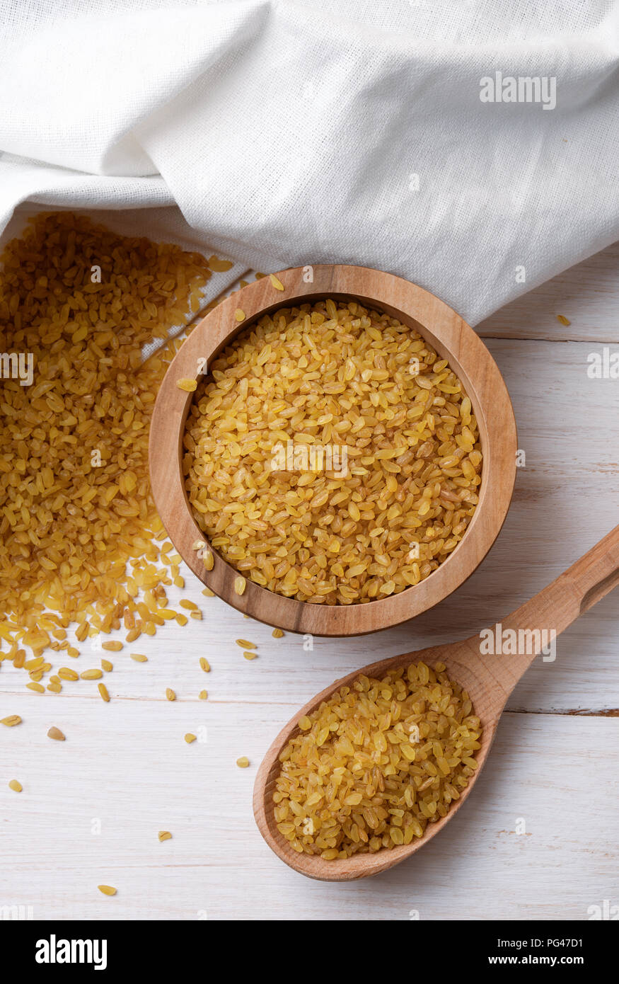 Vista in pianta secca di Bulgur di grano nella ciotola e cucchiaio su sfondo di legno. Foto Stock