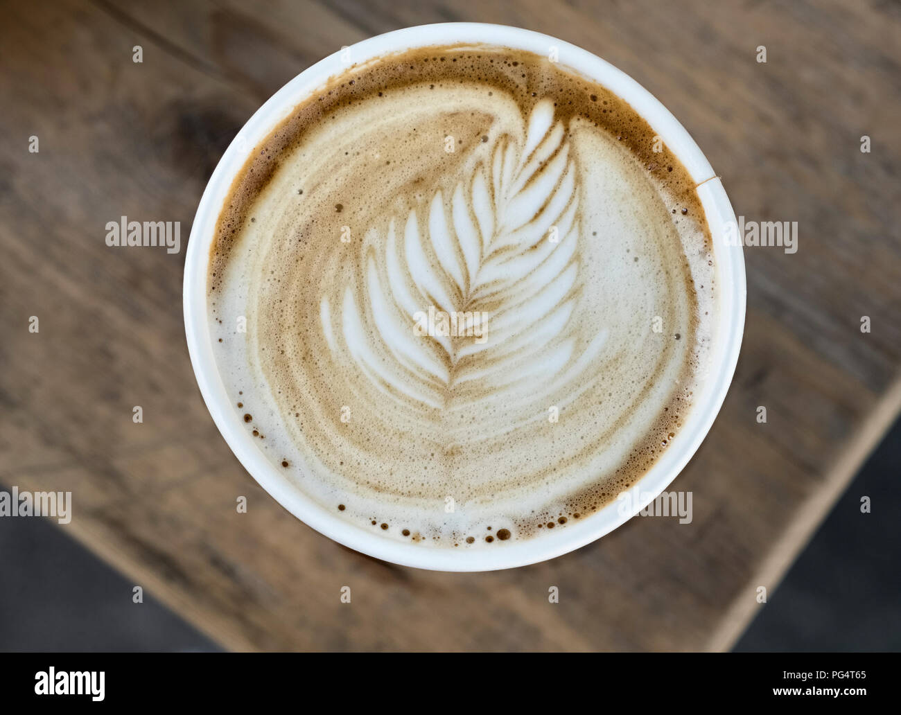 Cappuccino caffè in un bicchiere di carta, con un pattern di foglia sulla superficie della schiuma di latte Foto Stock