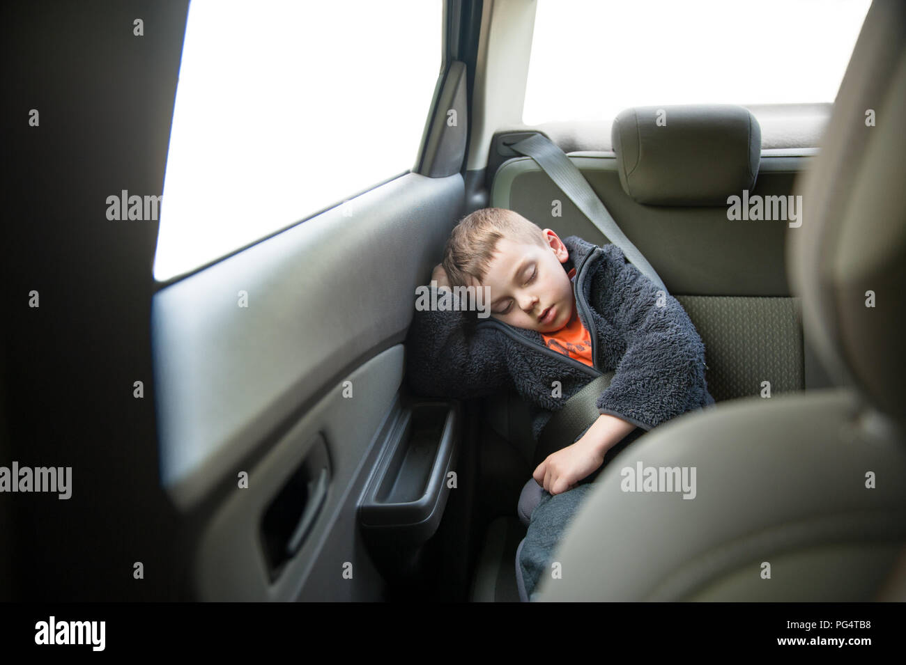 Piccolo grazioso capretto caucasica indossando vestiti caldi dormire in auto interno indossare cintura di sicurezza Foto Stock