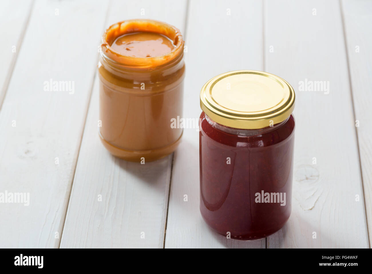 Burro di arachidi e vasi di marmellata, close-up. Luce di tavole di legno dello sfondo. Foto Stock