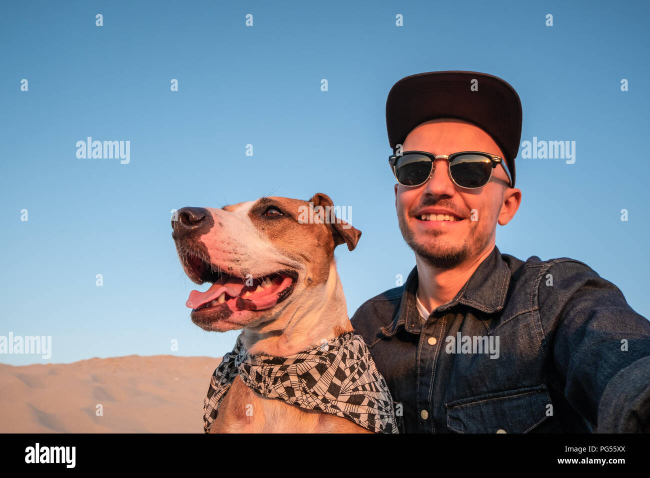 Uomo prendendo un selfie con cani sulla spiaggia sabbiosa. Felice giovane maschio persona fa autoritratto con il suo cane all'aperto Foto Stock