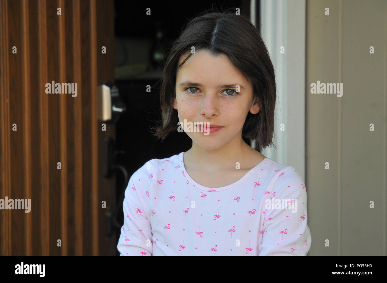 Giovani blue-eyed ragazza sorridente, in piedi di fronte ad aprire la porta di casa. Diretto e invitando a guardare con un leggero sorriso. Foto Stock