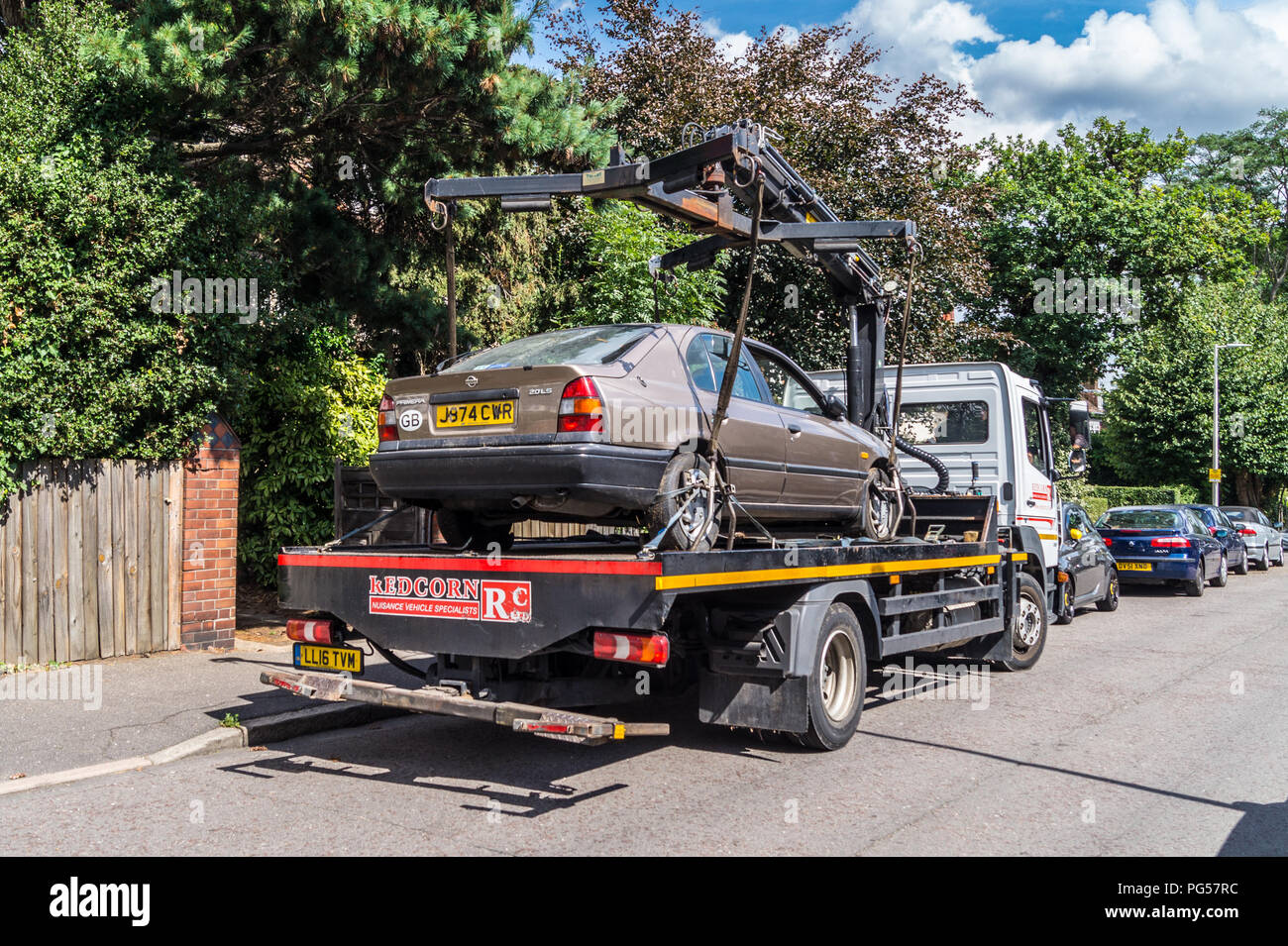 Un 1992 Nissan Primera 2.0 LSI berlina automatico auto viene sollevato al di sopra di una Mercedes Atego camion di recupero per il riciclaggio, South Woodford, Londra, Inghilterra Foto Stock