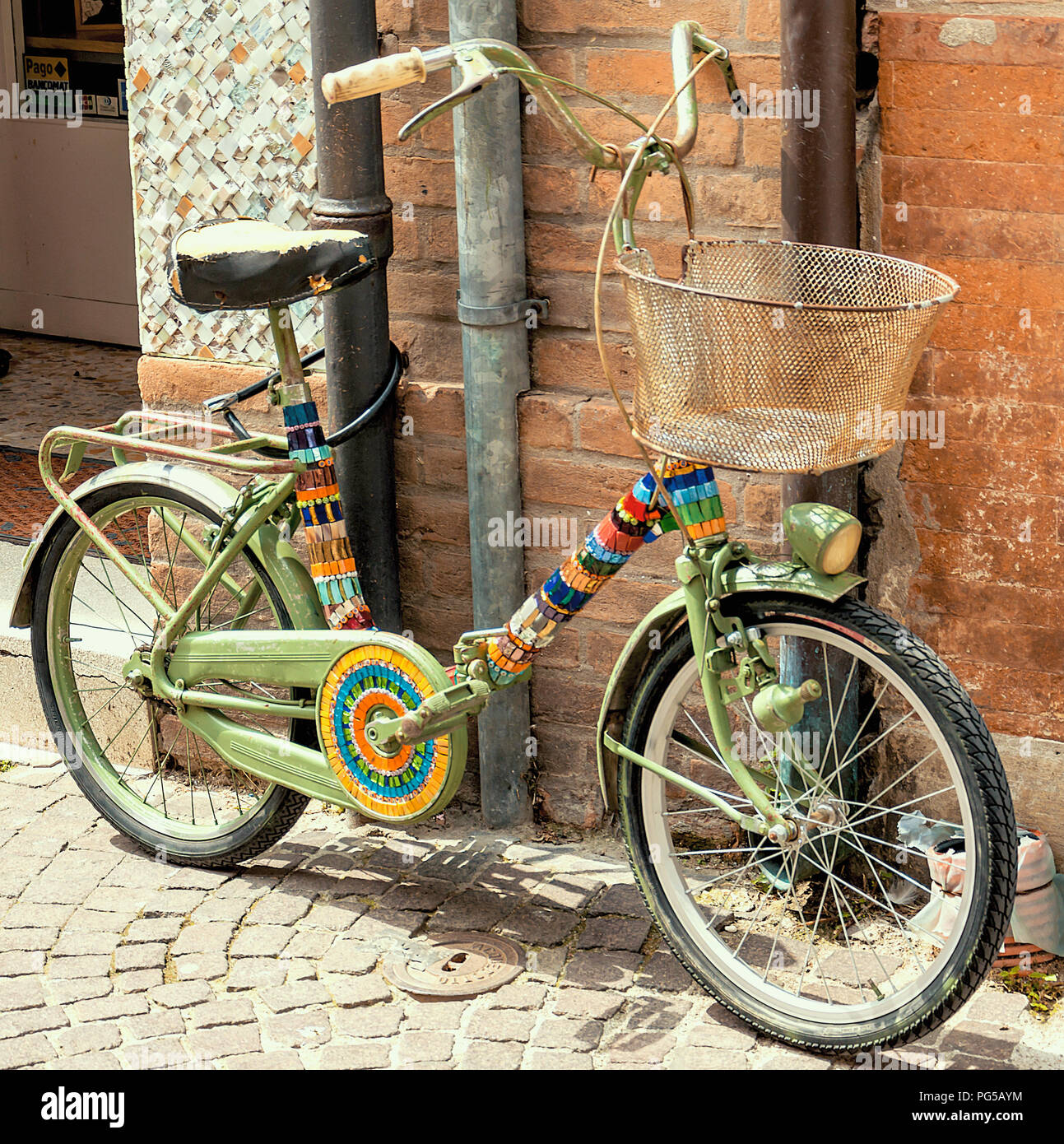 Poco colorati bicicletta legato con un lucchetto a un tubo al lato di una strada Foto Stock